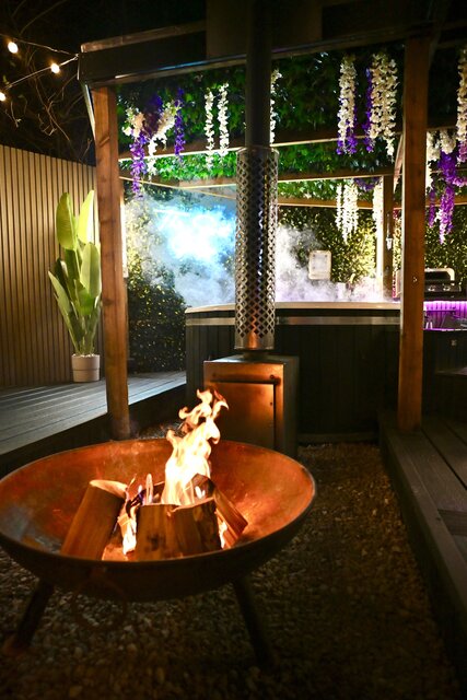 “Close-up of a roaring outdoor log-burning fire beside a luxury hot tub, highlighting the warmth, glow, and indulgent atmosphere of this relaxing outdoor space.”