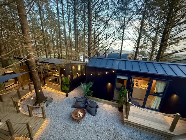 Daytime birds-eye view of The Vista outdoor area at The Secret Garden Glamping showing the firepit, a tree, and string lighting throughout, creating a stylish, inviting, and luxurious setting.