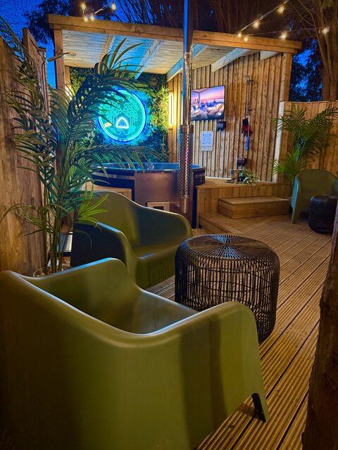 Luxury glamping outdoor area with covered hot tub, wall-mounted smart TV, comfortable seating and stylish artificial jungle-themed decor at The Secret Garden Glamping.