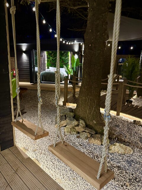 The Vista outdoor area at The Secret Garden Glamping featuring swings with a tree in front, and the bedroom area visible in the background, creating a playful, stylish, and luxurious setting