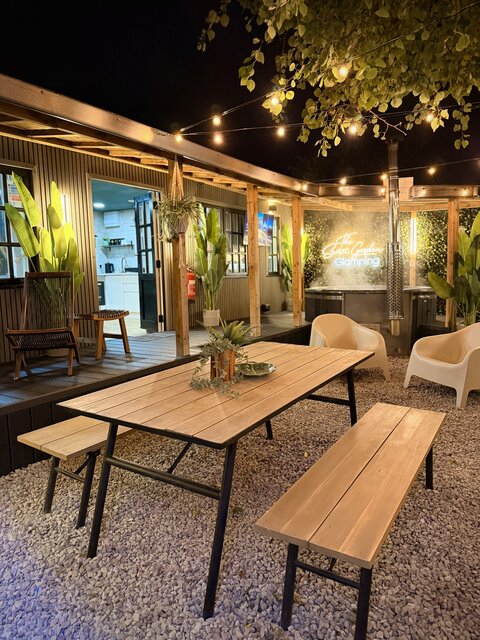 Outdoor glamping area featuring a wooden picnic bench decorated with tropical plants, a private hot tub, stylish decking and the main entrance doors leading in the unit at The Secret Garden Glamping
