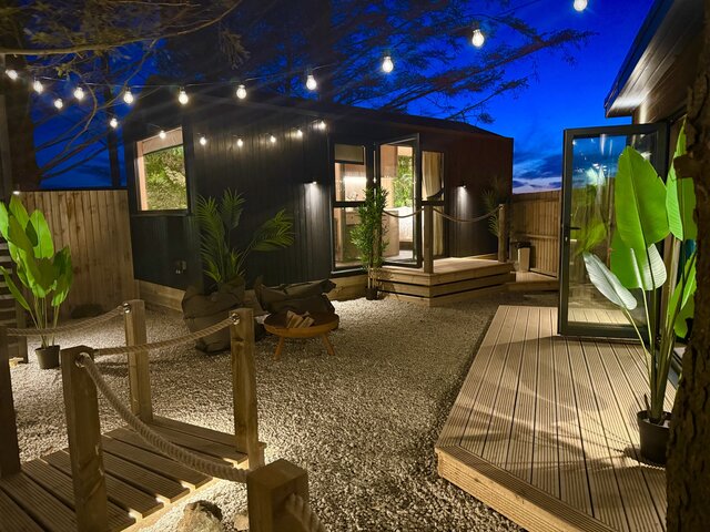 The Vista bedroom exterior at The Secret Garden Glamping at night, featuring plants throughout, string lighting overhead, floor lighting, and a night sky above, creating a stylish atmosphere.