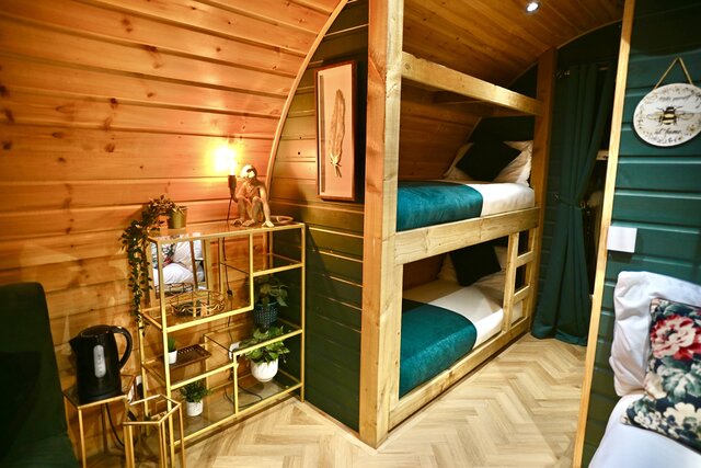 “The Keep bedroom at The Secret Garden Glamping featuring a perfectly made double bed and two single bunk beds, beautifully lit and styled with plants and decorative artwork for a cozy atmosphere