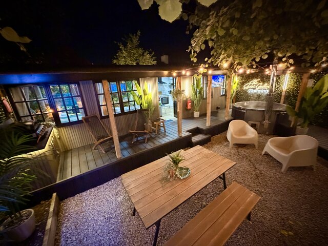 The Lodge outdoor area at The Secret Garden Glamping with private hot tub, wooden picnic bench, spacious decking, and large windows showing the cozy interior for a warm, luxurious stay