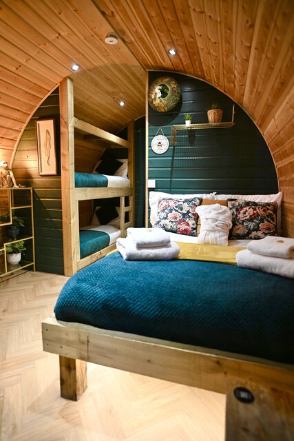 “The Keep bedroom at The Secret Garden Glamping featuring a perfectly made double bed and two single bunk beds, beautifully lit and styled with plants and decorative artwork for a cozy atmosphere