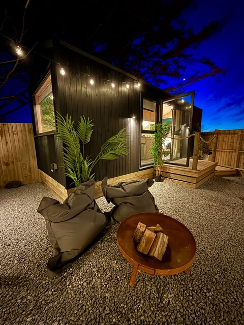  The Vista outdoor area at The Secret Garden Glamping featuring a firepit with two seats behind it, flanked by two plants, under a beautiful night sky, creating a cozy, stylish, and luxurious setting