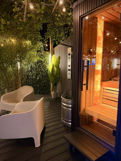 Close-up view of the outdoor sauna area featuring the wooden sauna entrance, modern outdoor shower, natural greenery and luxury detailing at The Lodge, Secret Garden Glamping
