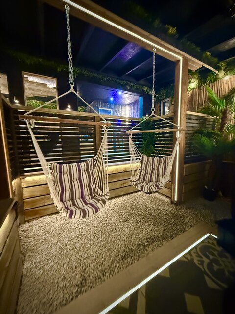 “The Pavilion outdoor area at The Secret Garden Glamping featuring two striped swinging chairs, surrounded by lush greenery and elegant landscaping, creating a beautiful and luxurious setting.