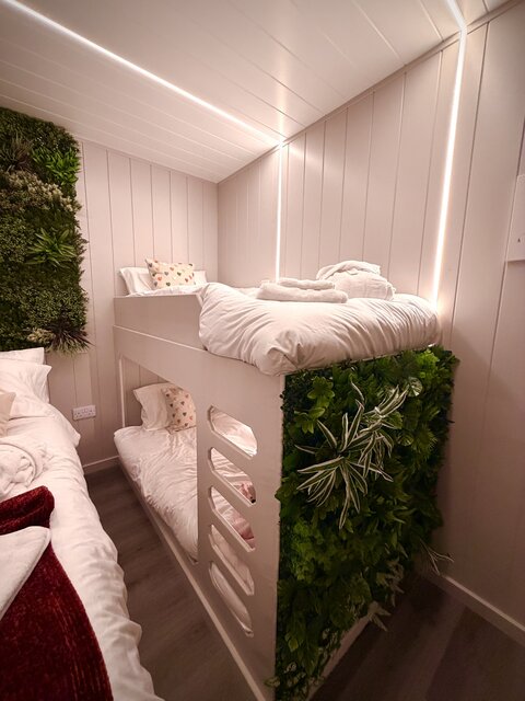 “A pristine bunk bed at The Secret Garden Glamping, featuring perfectly made white sheets that look inviting and comfortable. The lower section of the bunk is adorned with a garden-inspired feature.