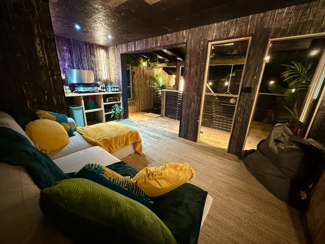"Interior of a luxury glamping pod at The Secret Garden Glamping, showing two perfectly made, cozy beds in a wooden-style area, opening up to the full pod with a green sofa and compact kitchen.