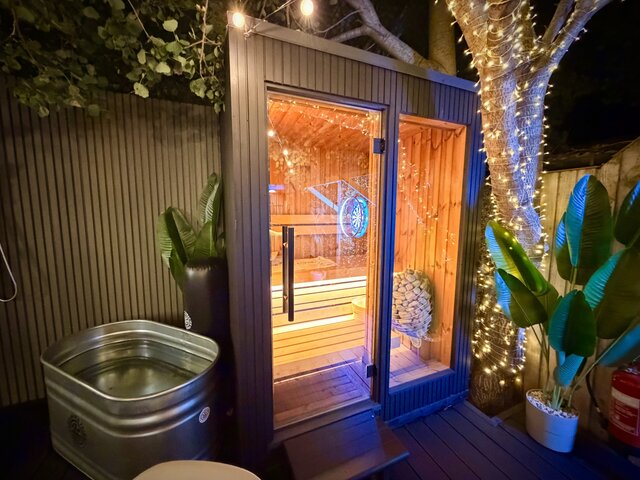 Close-up view of the outdoor sauna area featuring the wooden sauna entrance, modern outdoor shower, natural greenery and luxury detailing at The Lodge, Secret Garden Glamping.