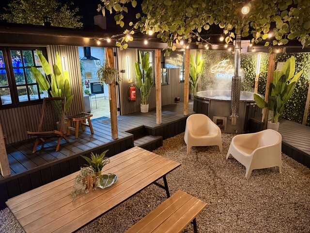 Outdoor area with picnic table and hot tub on decking, with a view into the modern kitchen area through the main door at The Secret Garden Glamping.