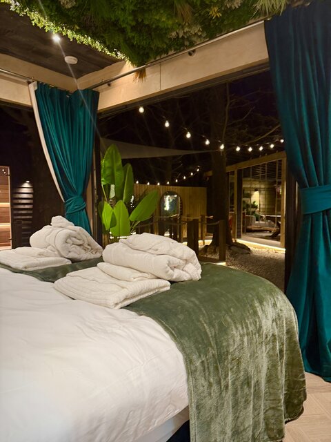 The Vista bedroom interior at The Secret Garden Glamping featuring a neatly made bed with a view of the outdoor area, including a tree, nighttime string lighting, and ambient lighting.