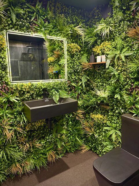 Modern luxury bathroom with a jungle-leaf feature wall, black toilet and matching sink, illuminated mirror with green LED lighting, and stylish contemporary décor at The Secret Garden Glamping.