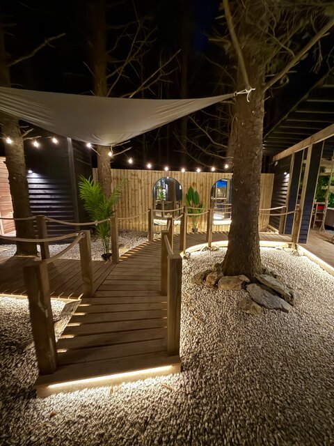 The Vista outdoor area at The Secret Garden Glamping illuminated by floor lights, featuring a tree and surrounding plants in the background, creating a vibrant, stylish, and luxurious outdoor space.