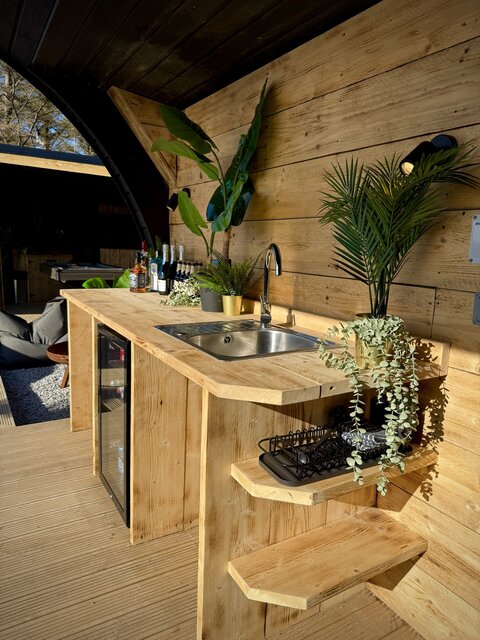“Horizon pod bar area at The Secret Garden Glamping featuring a stylish selection of liquors and drinks for cocktail making, with lush greenery and plants behind the bar.