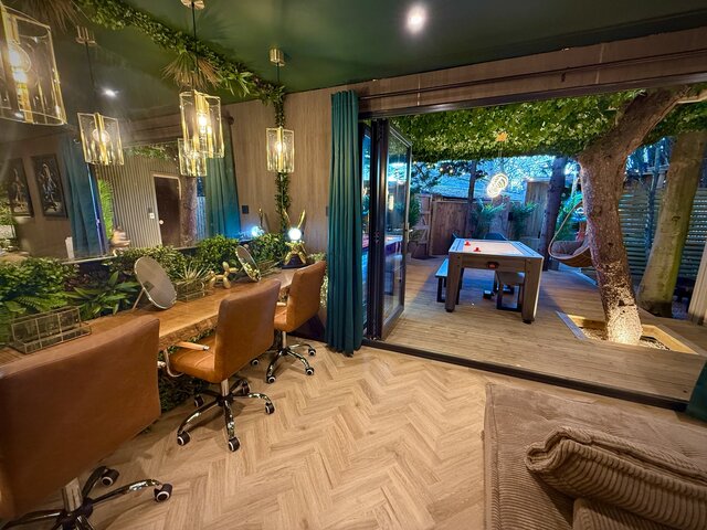 Luxury glamping interior with three stylish makeup stations, a large sliding door leading to the outdoor space, a brown velvet pouf, and elegant beige chevron flooring at The Secret Garden Glamping