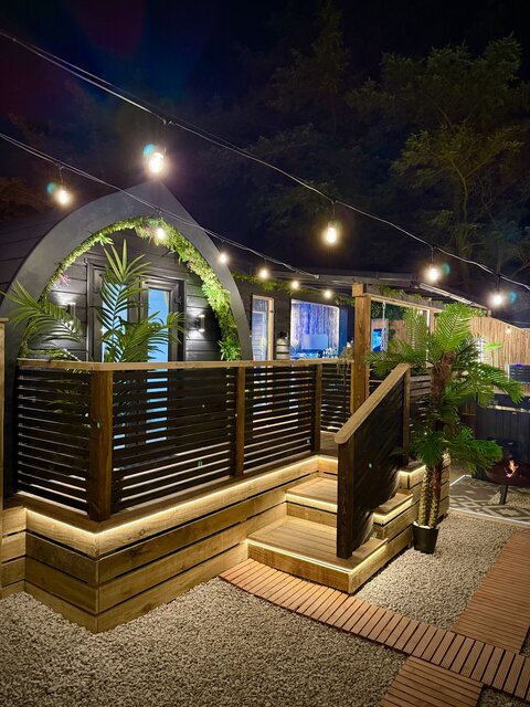 “Night time exterior of the Pavilion at The Secret Garden Glamping, showcasing the pod in all its beauty with illuminated steps leading up to the entrance, creating a warm, inviting, atmosphere.