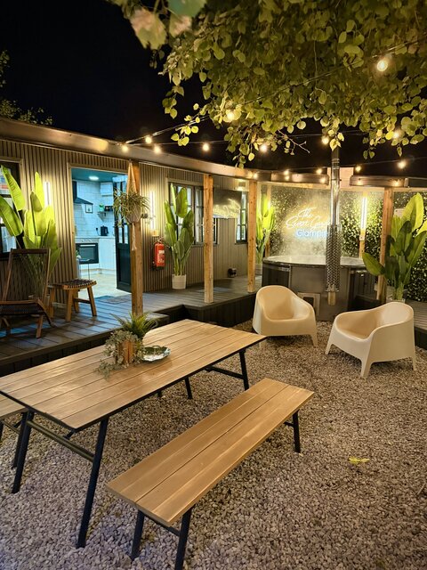 Sheltered outdoor area featuring a wooden picnic bench decorated with plants, offering a cosy and inviting space for guests to relax at The Secret Garden Glamping