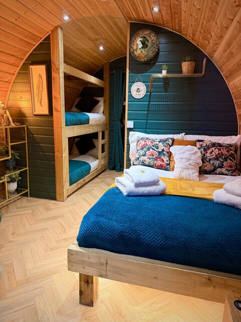 “The Keep bedroom at The Secret Garden Glamping featuring a perfectly made double bed and two single bunk beds, beautifully lit and styled with plants and decorative artwork for a cozy atmosphere