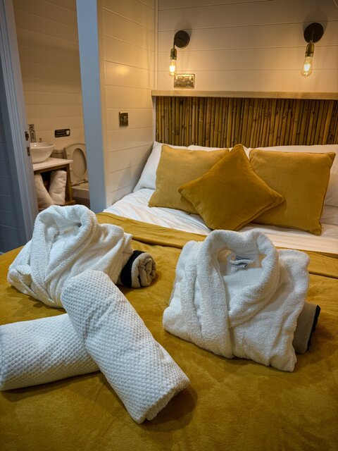 “A cozy bedroom at The Pavillion featuring a neatly made bed with mustard-yellow bedding and matching cushions. Creating a comfy and relaxing nature.