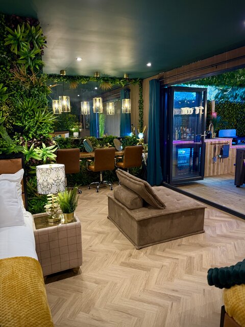 Luxury glamping suite with a cosy bed, jungle-style plants, a brown velvet chair, a modern bathroom with a glass-door shower, and three individual makeup stations at The Secret Garden Glamping.
