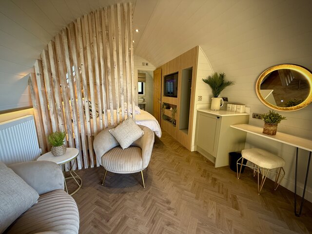 “Wider view of the Horizon pod bedroom at The Secret Garden Glamping, featuring a cozy and inviting seating area with a central table, a large illuminated mirror above, and a view of the bedroom.