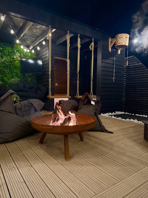 “The Cove outdoor area at The Secret Garden Glamping showcasing a dramatic, roaring fire with vibrant red flames, surrounded by sumptuous, plush bag-style seating for maximum comfort.