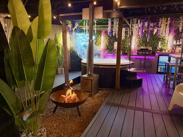 “Roaring outdoor log-burning fire beside a luxury hot tub, perfectly complementing each other to create a warm, indulgent, and inviting outdoor experience.”