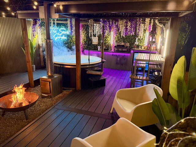 “Roaring outdoor log-burning fire beside a luxury hot tub, perfectly complementing each other to create a warm, indulgent, and inviting outdoor experience.”