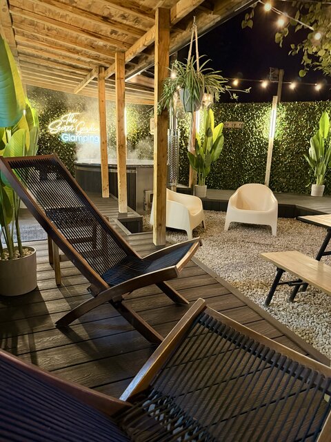 Outdoor relaxation area featuring two brown folding deck chairs on wooden decking, a picnic bench with plants and a private hot tub all set within a cosy sheltered space at The Secret Garden Glamping