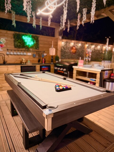 “The Blossom pod’s pool table elegantly set for a game, with gleaming balls and cues arranged perfectly. Ambient lighting accentuates the polished surface, while in the background a sleek bar area.
