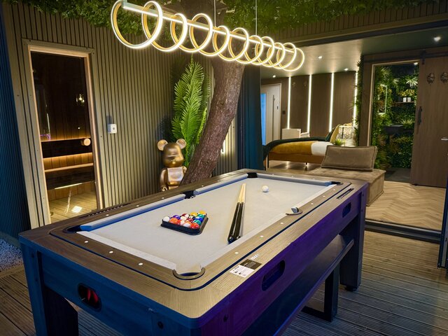 Luxury outdoor space featuring a convertible pool table that transforms into an air hockey and dining table, swirl lighting overhead and stylish decking flooring at The Secret Garden Glamping.