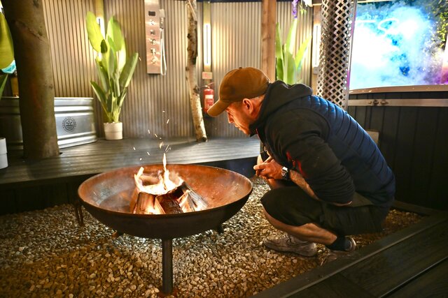 “The site manager tending the outdoor fire pit, ensuring the flames are perfect and inviting, ready for guests to enjoy a cosy, luxurious evening at The Secret Garden Glamping.”