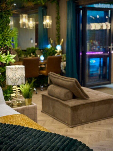 Luxury bedroom with cozy double beds, brown velvet pouf, soft ambient lighting, and large double doors opening onto a private outdoor area at The Secret Garden Glamping.