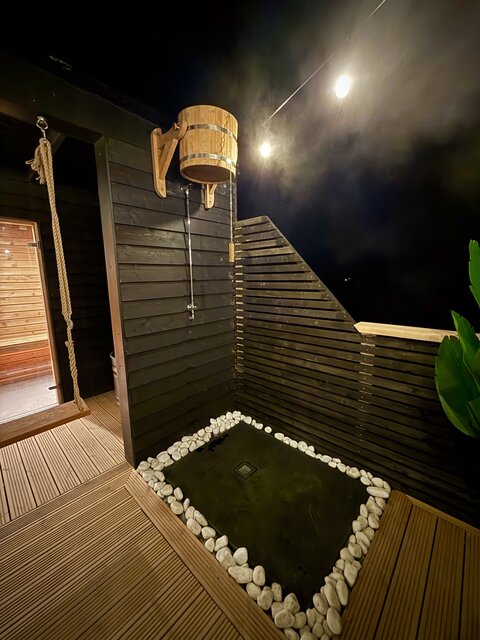 Luxurious outdoor space featuring a Swedish bucket shower with sleek jet-black flooring, soft white pebbles surrounding the base, and the dark night sky enhancing the elegant, high-end glamping atmos