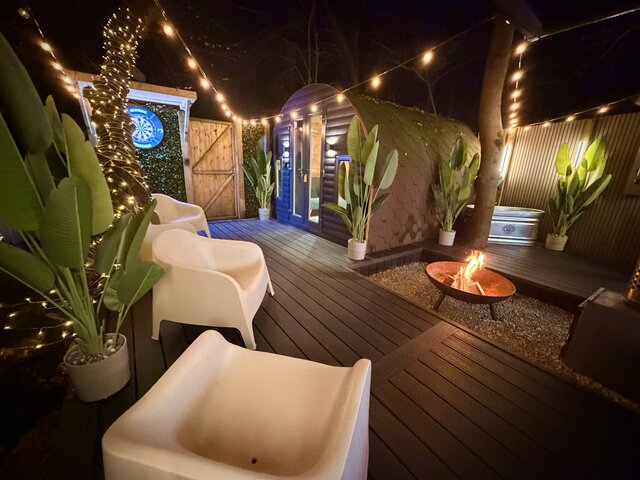 “Outdoor relaxation area featuring a glowing fire pit, luxury white chairs, and a dartboard in the background, creating a cozy and inviting space to unwind and enjoy the evening.”