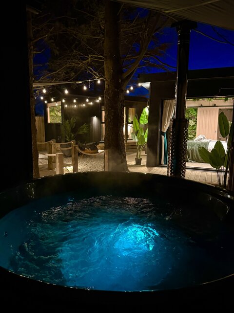 This photo is taken from the viewpoint of the hot tub, looking out across The Vista’s beautifully styled outdoor area. Soft lighting highlights the lush plants that frame the space.