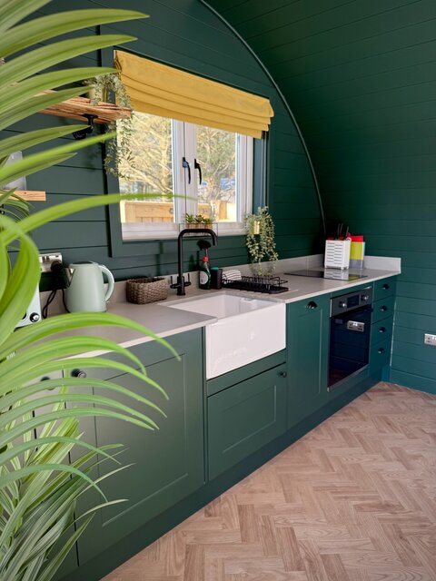 “The Cove kitchen area at The Secret Garden Glamping featuring a charming double window above the sink, luxury amenities including a kettle and oven, perfect for enjoying morning coffee.