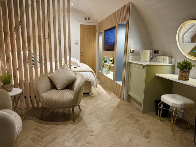 “The Horizon indoor bedroom at The Secret Garden Glamping, featuring a cozy and relaxing seating area with a central table, a large illuminated mirror above, and a view of the bedroom.