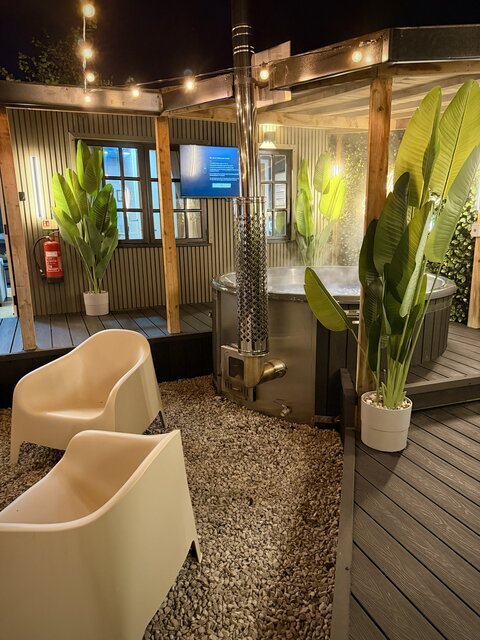 The Lodge outdoor area at The Secret Garden Glamping featuring a lit hot tub, two chairs, and plants throughout, creating a jungle-inspired, rustic, and luxurious atmosphere.