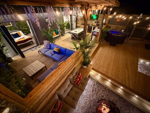 “Aerial view of the Blossom pod at The Secret Garden Glamping, highlighting its opulent outdoor space. Below, a firepit is surrounded by a bench with plush cushions, and an additional seating area.