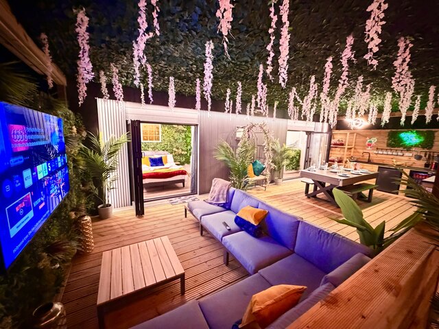 “The Blossom pod outdoor area at The Secret Garden Glamping, featuring two perfectly arranged couches around a luxurious coffee table that complements the golden-brown decking.