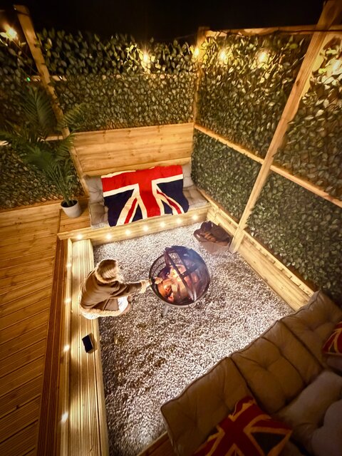 Aerial view of The Blossom pod’s firepit with a guest roasting marshmallows, surrounded by lush plant-grown fences. The warm glow of the fire highlights the cozy, and luxurious outdoor setting