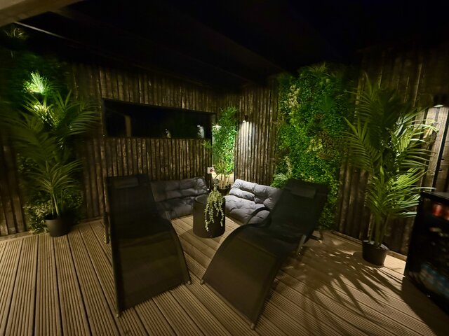 “Luxury outdoor relaxation area featuring two premium sun loungers and plush cushioned sofas surrounded by lush green plants, creating a serene spa-like atmosphere; the perfect cosy retreat.