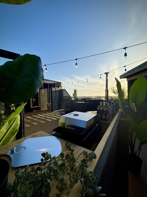 “The Cove outdoor area at The Secret Garden Glamping featuring a sleek jet-black hot plate griddle with a pizza oven attachment, sparkling hanging lights above, and a log-burning hot tub.