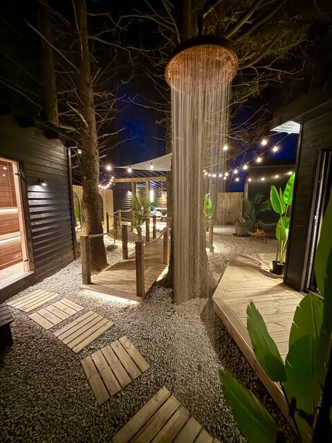 Outdoor shower at The Vista with water running under the night sky, framed by soft string lighting, lush plants, and the stylish exterior of the unit, creating a serene and luxurious open-air moment.