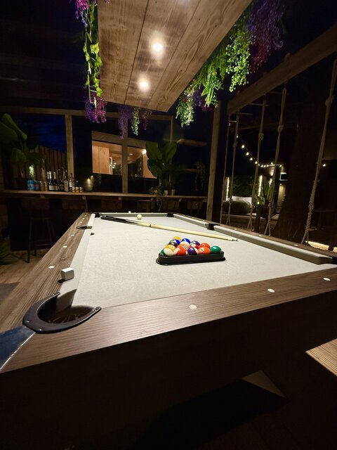 The Vista outdoor area at The Secret Garden Glamping featuring a pool table illuminated by overhead lights, creating a vibrant, stylish, and luxurious entertainment space.
