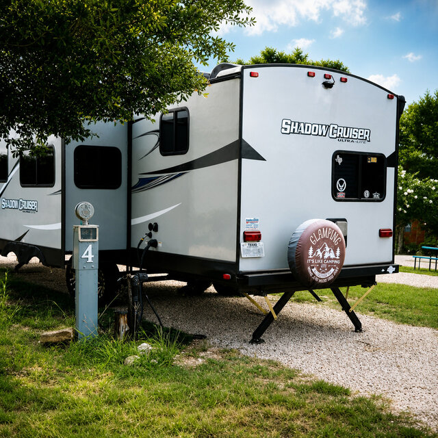 Spacious pull‑through RV site #4 at Al’s Hideaway in Pipe Creek TX, shaded by trees with gravel pad and picnic table.