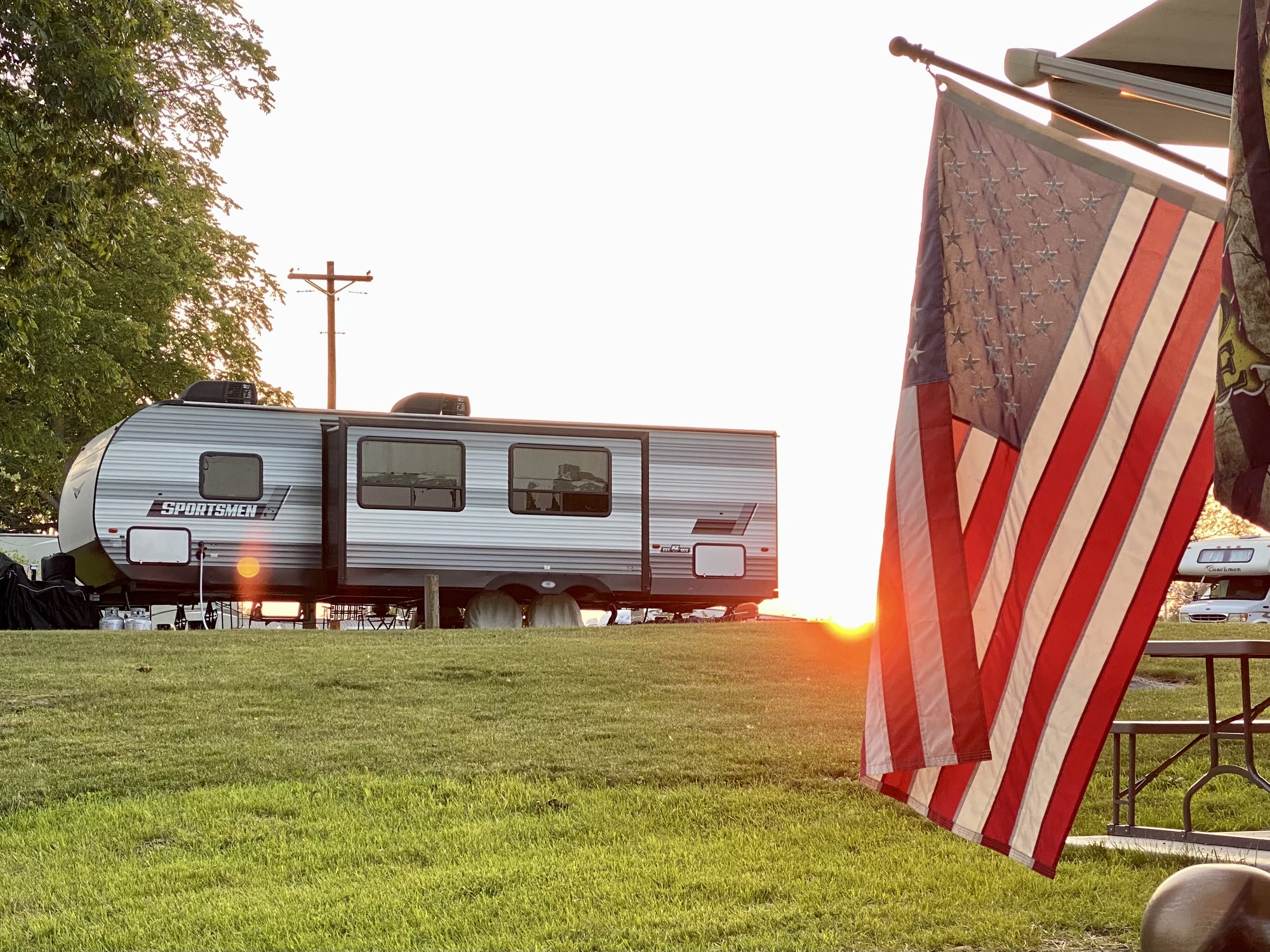 Camper with sunset in the background and American flag in foreground 